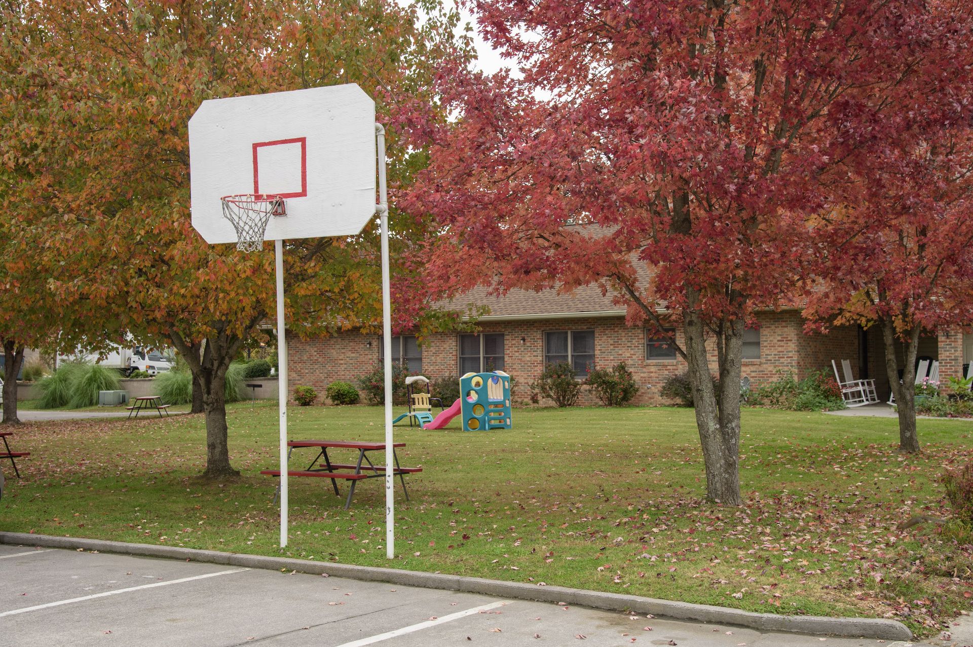 A basketball hoop and playground are in the grassy area in front of a brick building.
