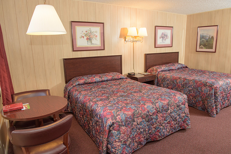 A hotel room with two beds, a table, chairs, and pictures on the walls.
